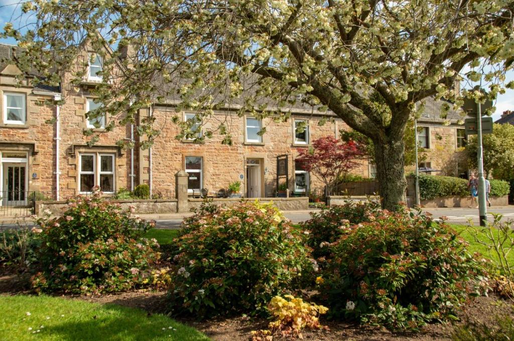 a large brick building with a tree and bushes at Room Only Corbies Rest in Inverness