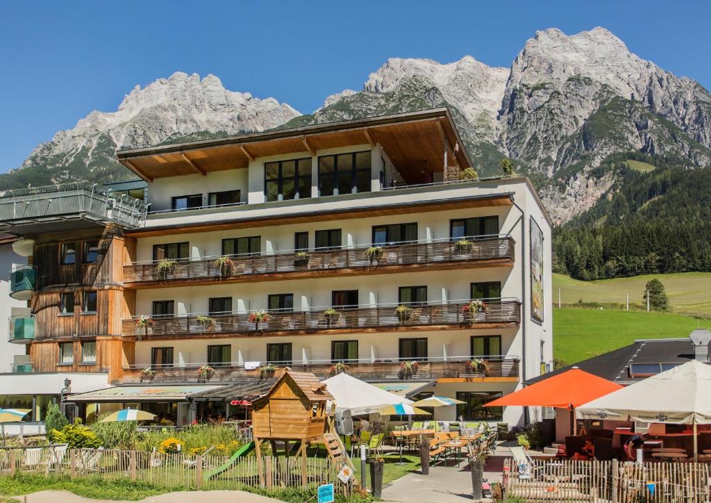 a hotel in the mountains with tables and umbrellas at Hotel Bacher Asitzstubn in Leogang