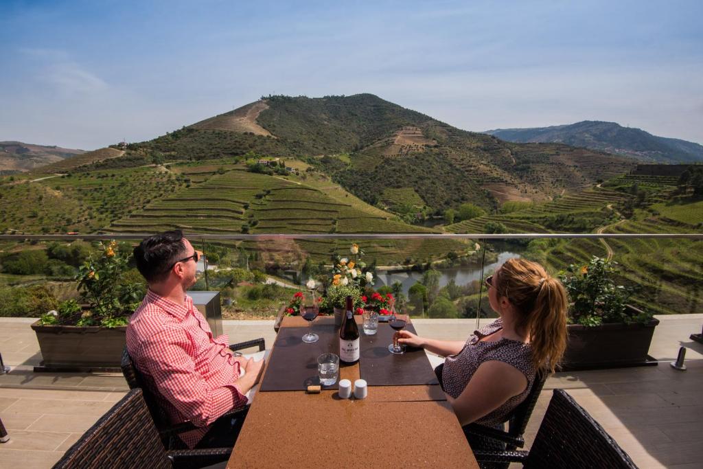 a man and woman sitting at a table with a view at Vila Gale Douro Vineyards in Armamar