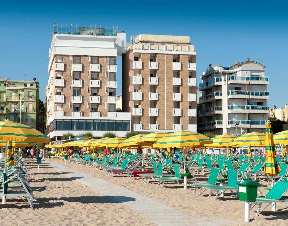 a beach with chairs and umbrellas and buildings at Hotel Napoleon in Gabicce Mare