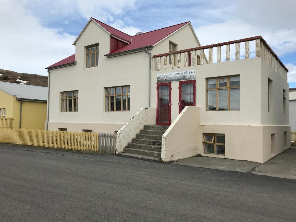 a white building with a red door on a street at Steinhúsið in Hólmavík