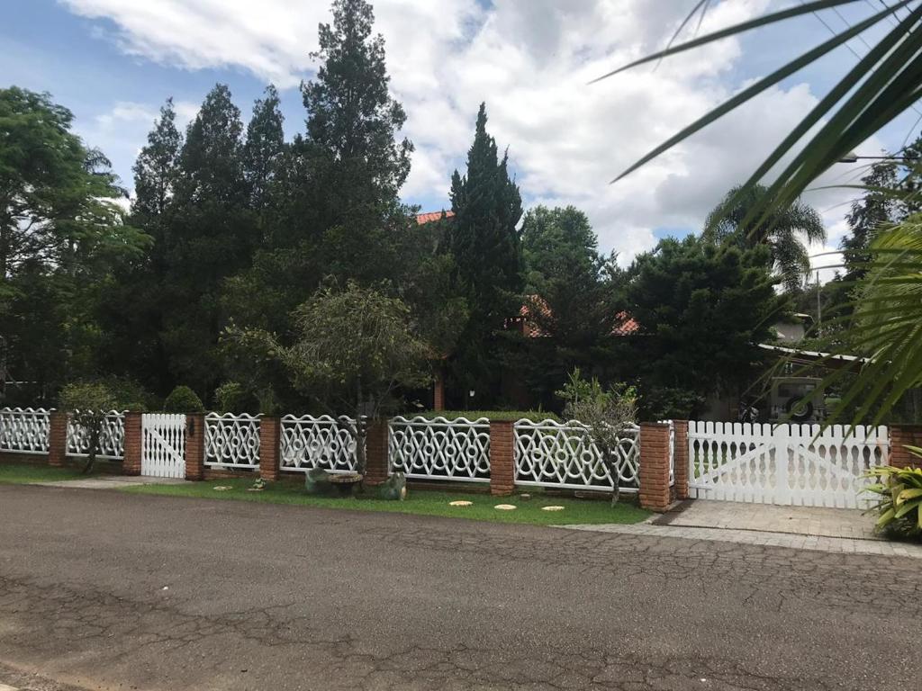 una cerca blanca frente a un patio con árboles en Casa alto padrão em condomínio fechado - São Roque, en Joaquim Egídio