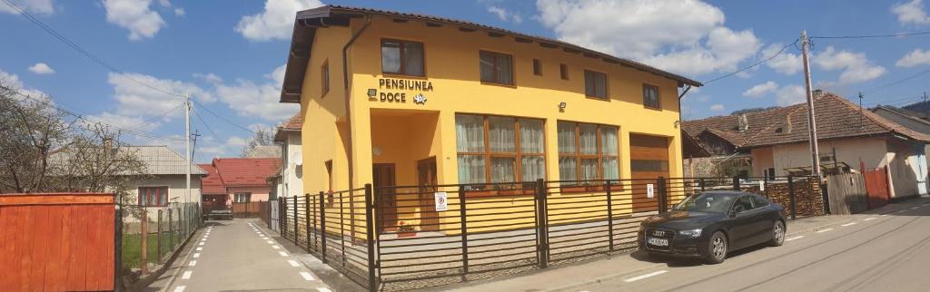 une voiture noire garée devant un bâtiment jaune dans l'établissement Pensiunea Doce, à Vişeu de Sus