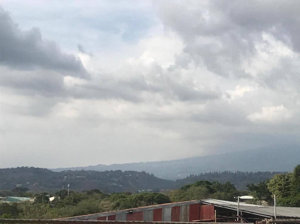 a cloudy sky with a building and mountains in the background at Casa del Suizo in Alajuela