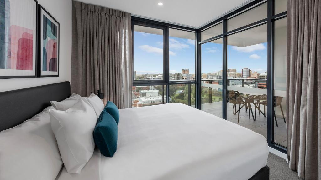 a bedroom with a white bed and a large window at Avani Adelaide Residences in Adelaide