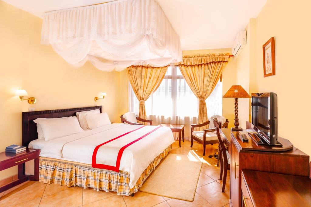 - une chambre avec un lit, un bureau et une télévision dans l'établissement New Safari Hotel, à Arusha