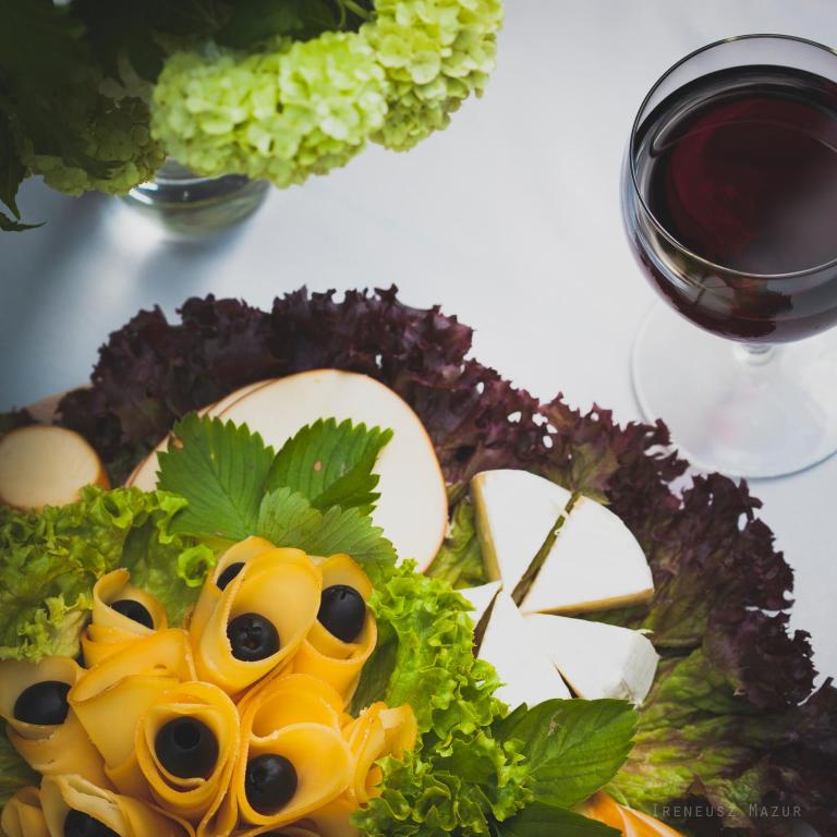 Cheese and olive platter arranged on lettuce with round brie and nearby glass of red wine.