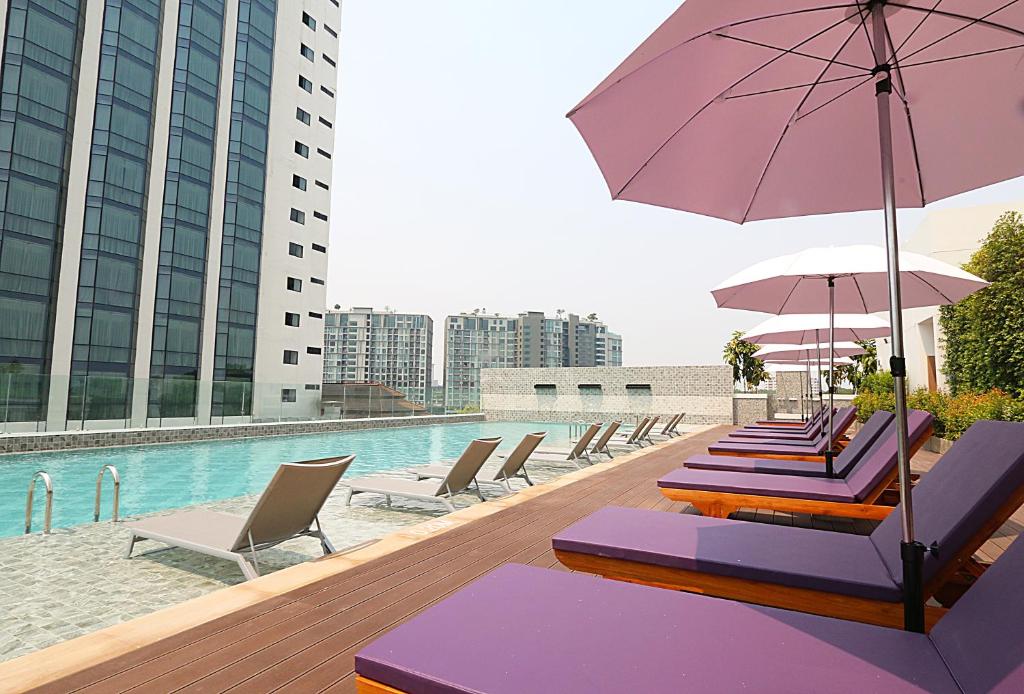 A sunny rooftop pool deck lined with purple loungers and pink umbrellas.