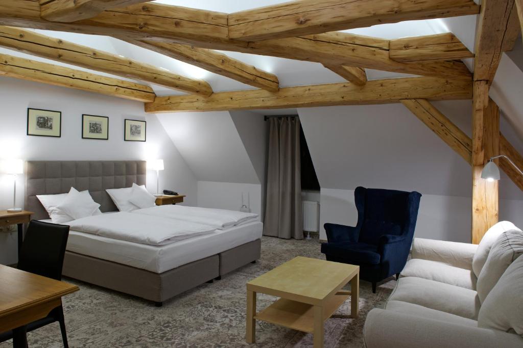 Spacious attic bedroom with exposed wooden beams, king bed, navy armchair, sofa, cozy modern ambiance