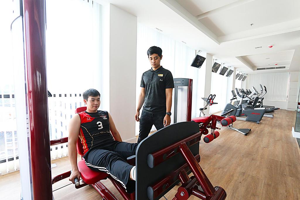 A bright hotel gym with strength equipment and cardio machines beside tall windows.