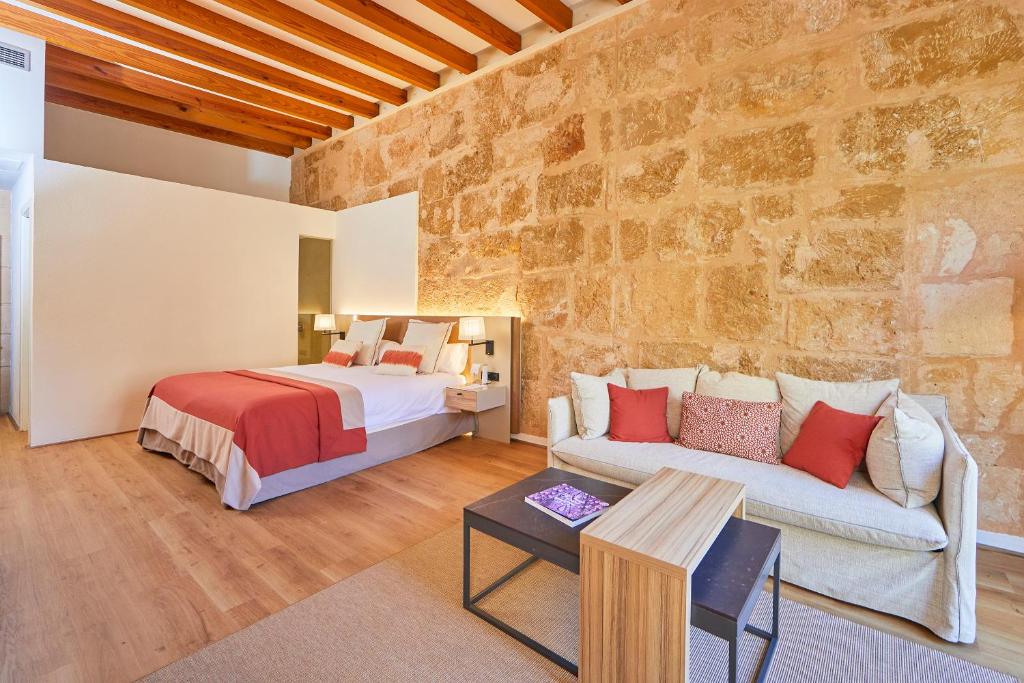 a bedroom with a bed and a couch in front of a stone wall at Santa Clara Urban Hotel & Spa in Palma de Mallorca