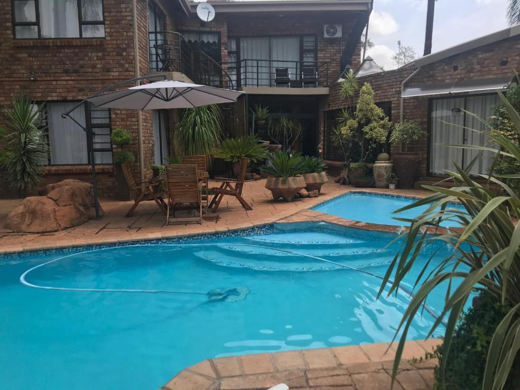 a swimming pool with an umbrella in front of a house at Francor Guesthouse in Pretoria