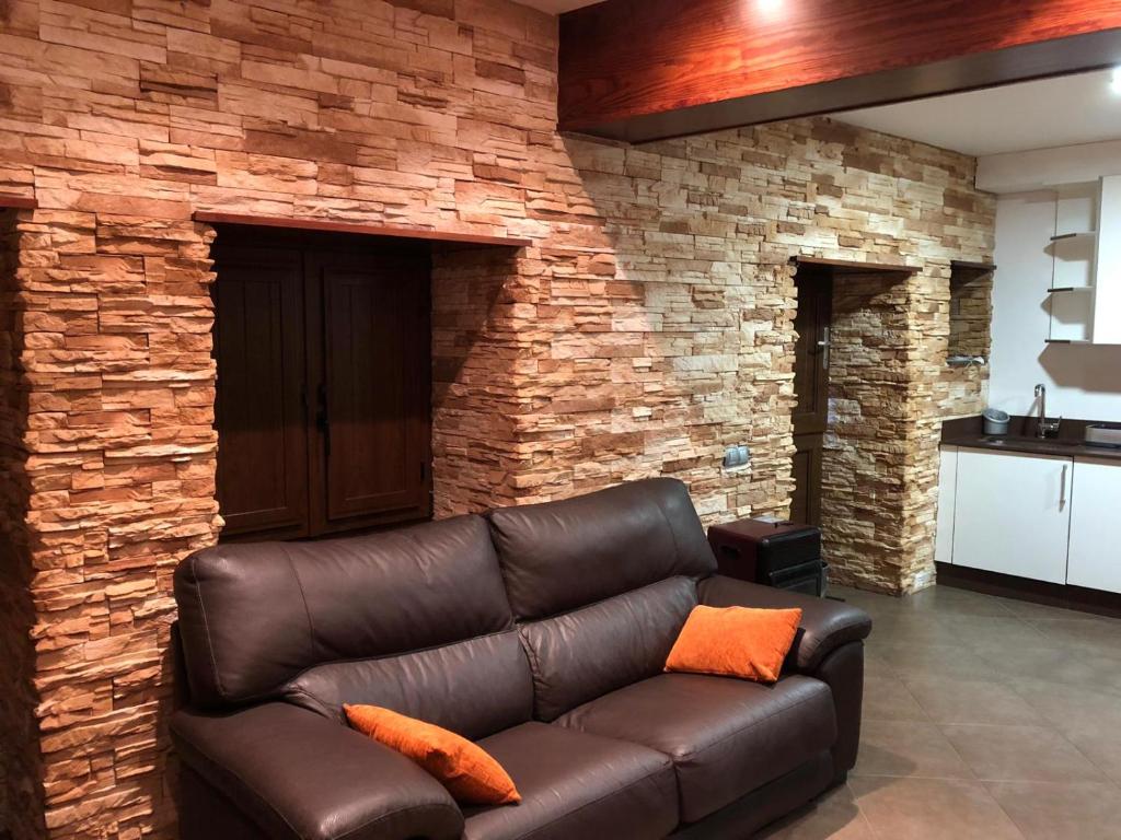 a leather couch in a living room with a brick wall at Vivienda de uso turístico, A Casa Do Campo in Fisterra