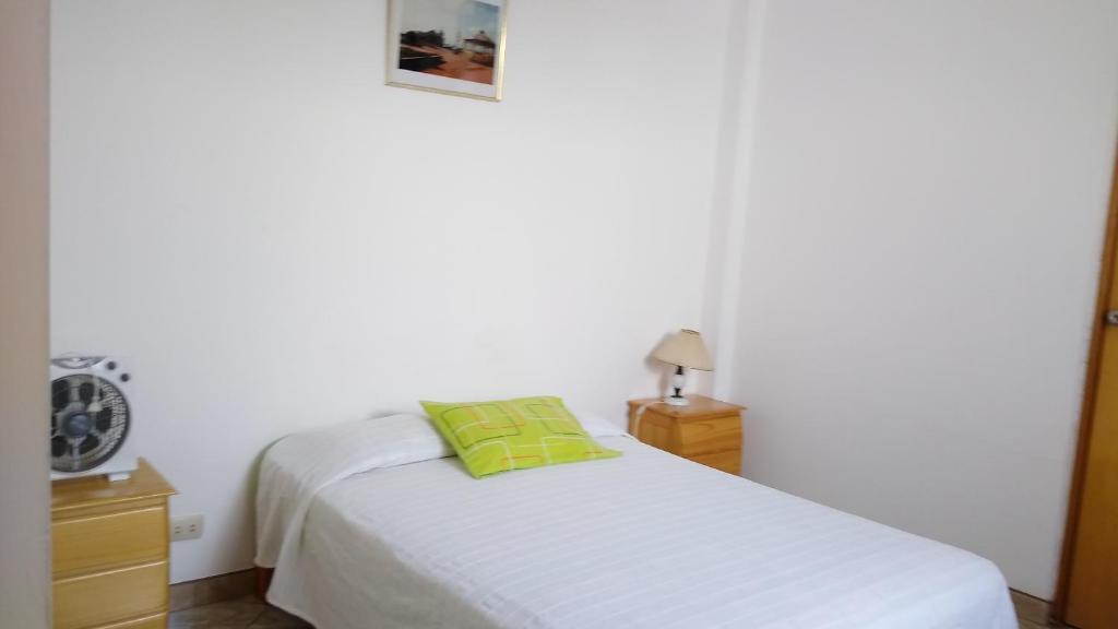 1 dormitorio con cama blanca y almohada verde en Hospedaje Puesta de Sol, en Salinas