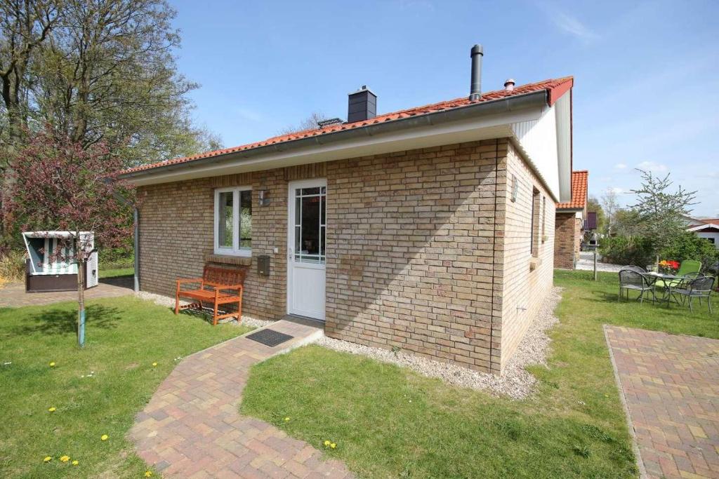 een klein bakstenen huis met een bank in een tuin bij Feriendorf Südstrand Haus 21 in Pelzerhaken