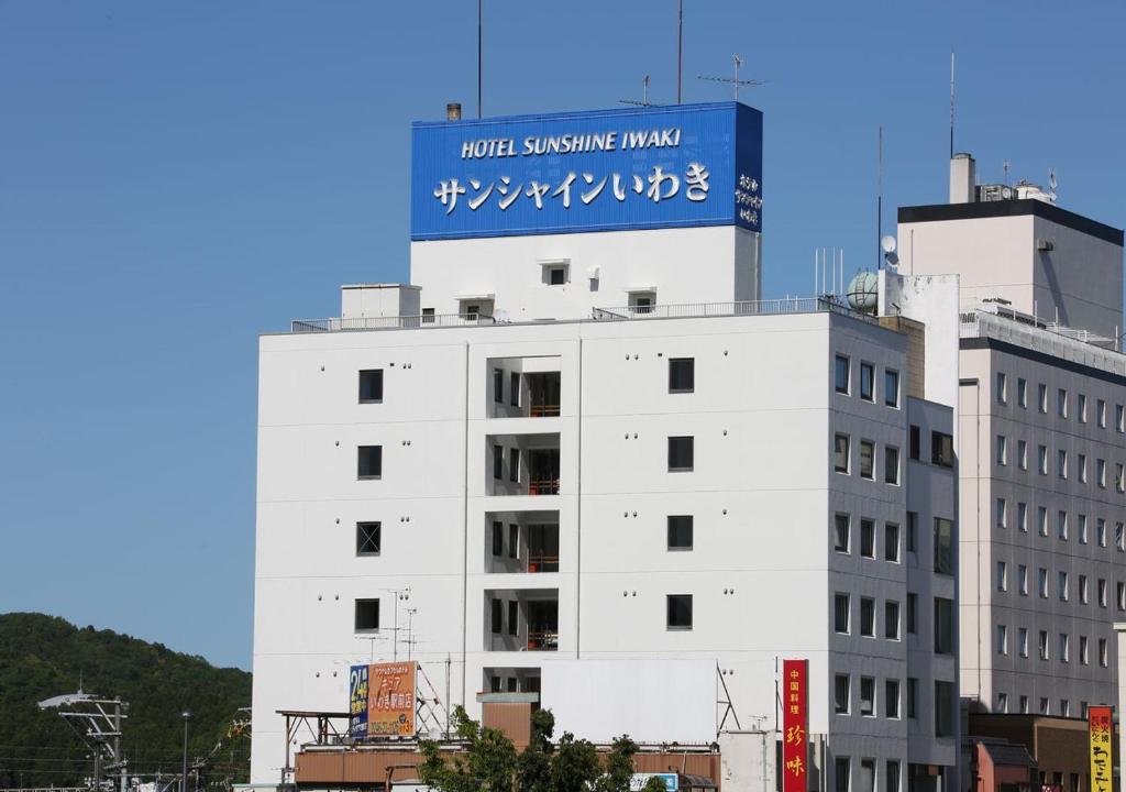 a white building with a blue sign on top of it at Hotel Sunshine Iwaki in Iwaki