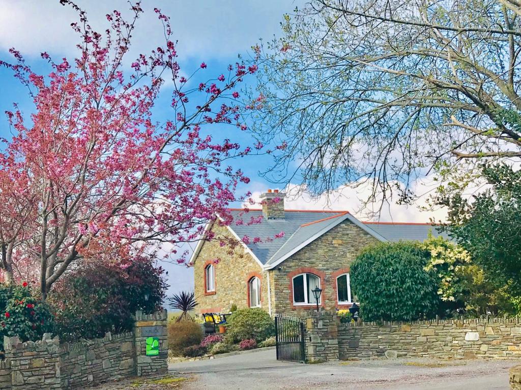 a brick house with a stone fence and trees at Niblick in Bantry