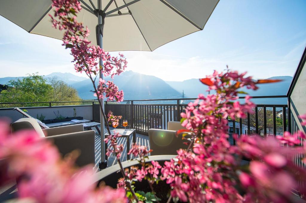 einen Balkon mit Tischen, Stühlen und rosa Blumen in der Unterkunft Hotel Zum Tiroler Adler in Dorf Tirol