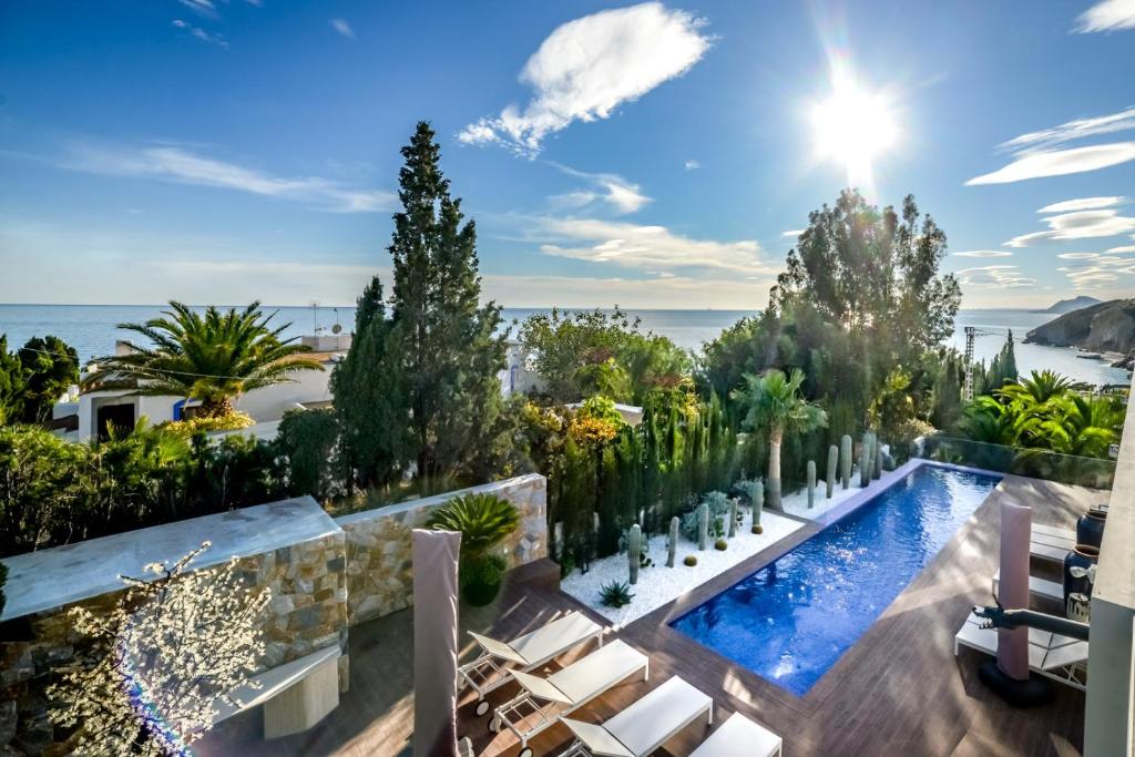 an outdoor swimming pool with chairs and trees and the ocean at Villa Carlota in Villajoyosa