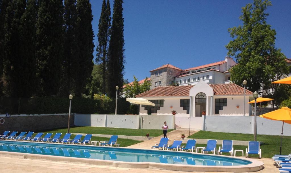 uma piscina com cadeiras azuis e um prdio em Hotel Urgeirica em Nelas