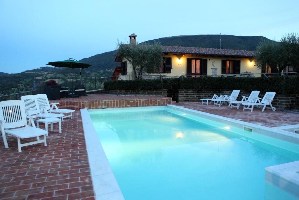 a swimming pool with white chairs and a house at Agriturismo Sole Luna in Piano Delle Pieve