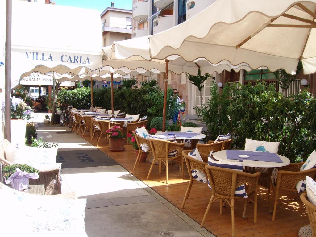 eine Außenterrasse mit Tischen, Stühlen und Sonnenschirmen in der Unterkunft Hotel Villa Carla in Grado