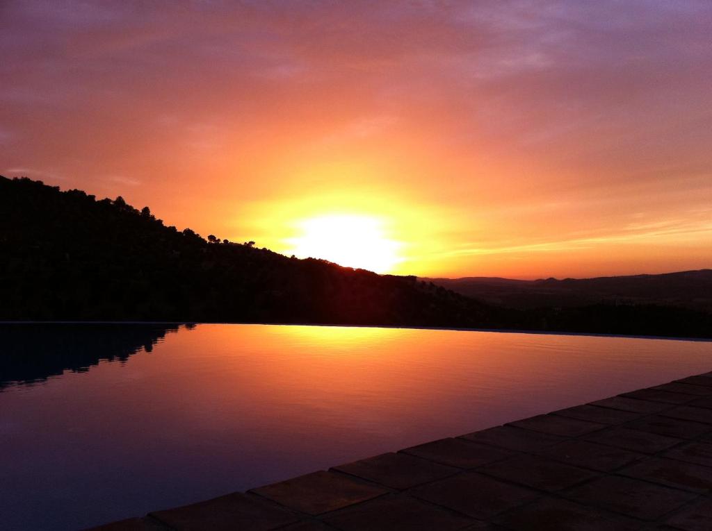 a sunset over a swimming pool with the sun setting at Hotel Rural los Tadeos in Zahara de la Sierra