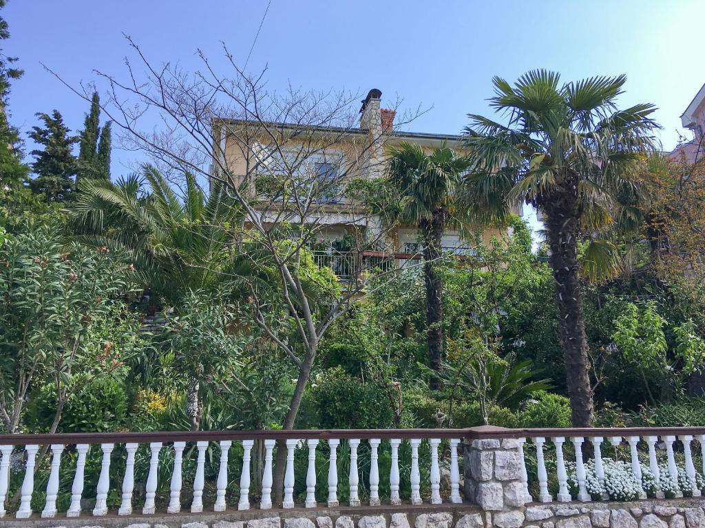 einen weißen Zaun vor einem Haus mit Palmen in der Unterkunft Apartments and Room Mirjana in Dramalj