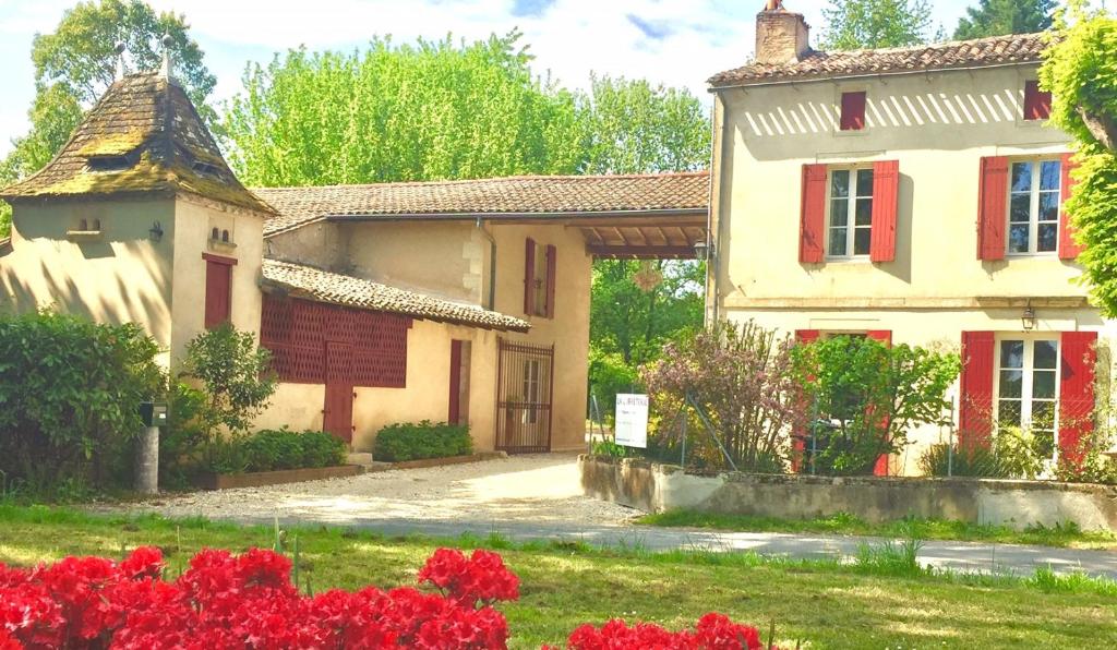 une maison avec des portes rouges et une cour ornée de fleurs rouges dans l'établissement LA CARRETERIE - Maison de Famille{s}, à Pineuilh