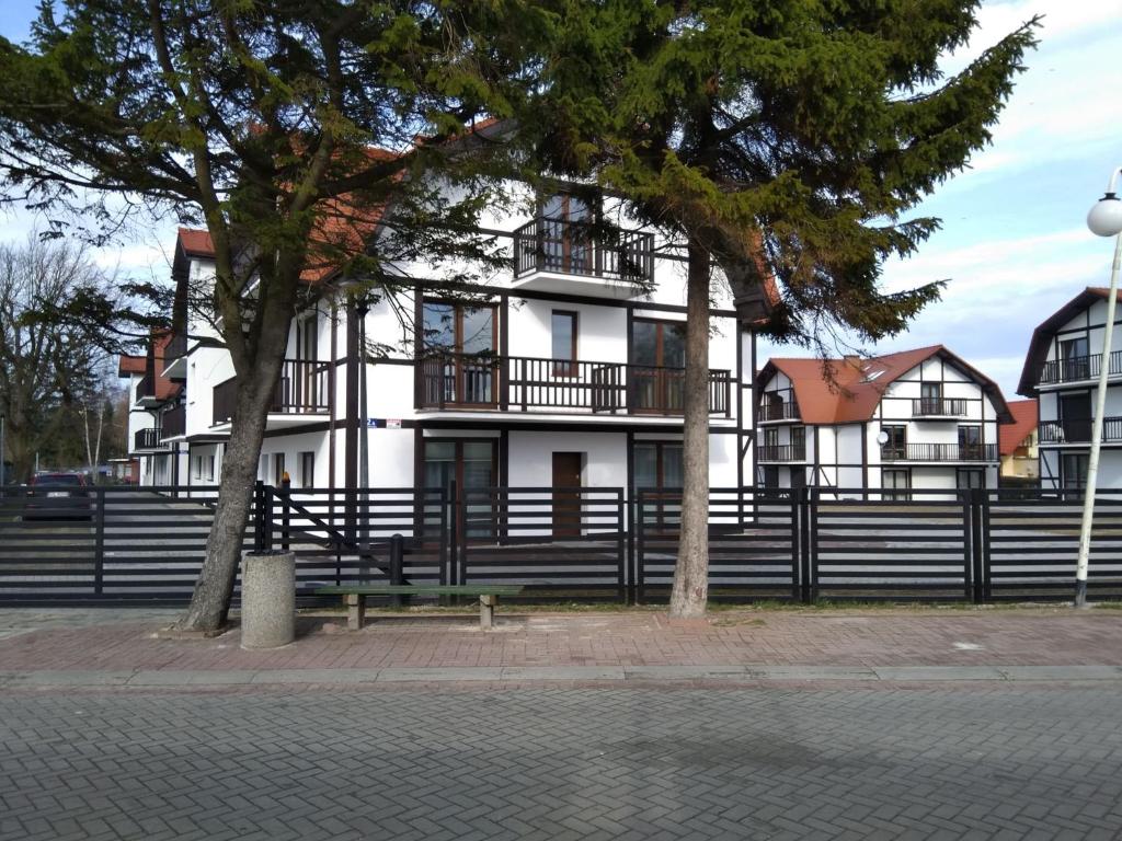 a white house with a black fence and trees at Apartamenty Bulwar Nadmorski, Rowy in Rowy