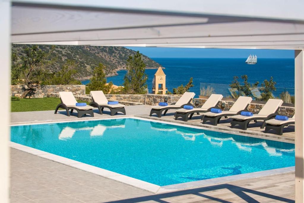 a pool with lounge chairs and a view of the ocean at Villa Bellelen in Agios Nikolaos