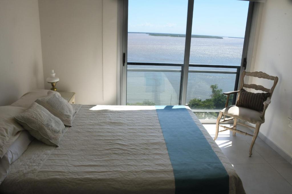 een slaapkamer met een bed en een stoel en een groot raam bij Torre Costanera Norte in Corrientes