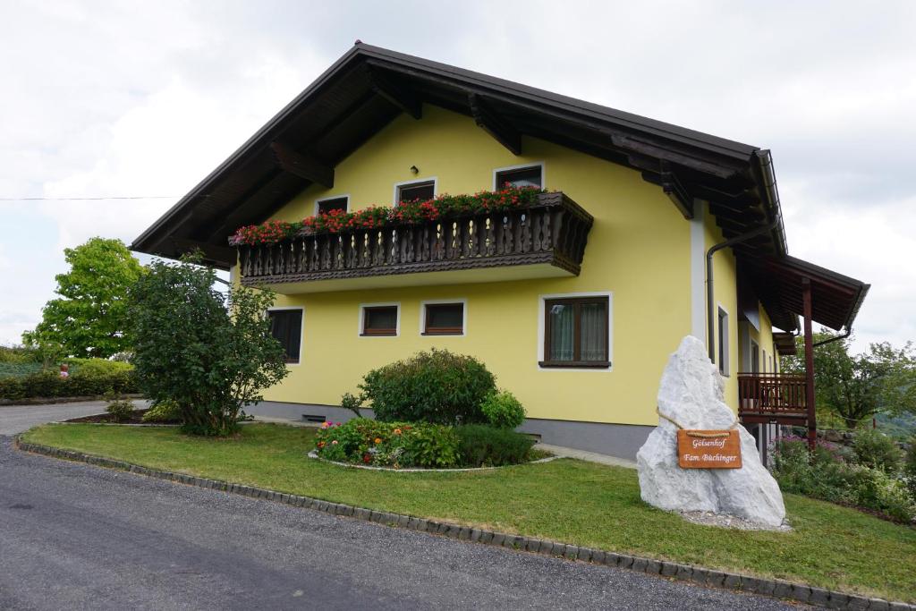 a yellow house with a balcony and a rock at Gölsenhof - Fam. Büchinger in Wald