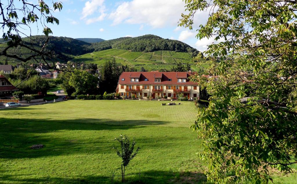 una casa grande en un campo verde con montañas en el fondo en Résidence Froehn, en Andlau