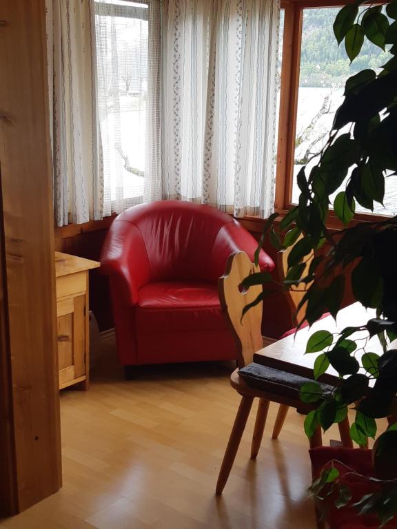 a red chair in a living room with a plant at Appartements direkt am See in Grundlsee