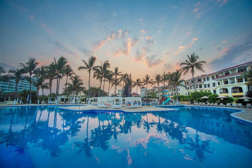 a large swimming pool with palm trees and a sunset at Samba Vallarta All Inclusive in Nuevo Vallarta 