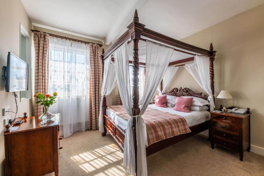1 dormitorio con cama con dosel y almohadas rosas en The White Hart Hotel, en Moretonhampstead