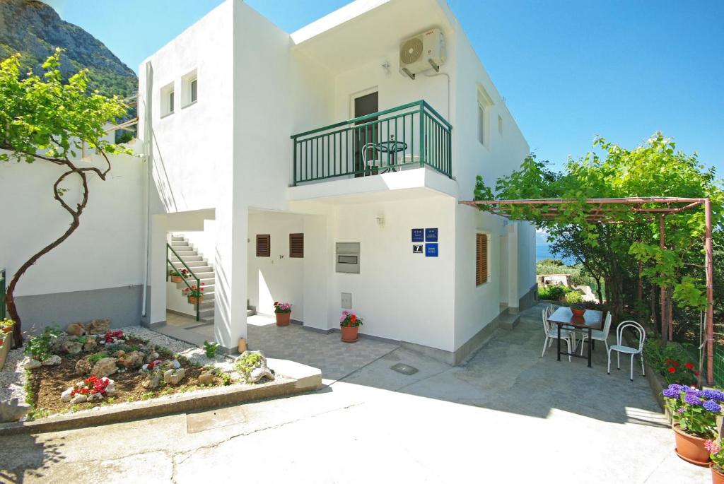 Cette maison blanche dispose d'un balcon, d'une table et de chaises. dans l'établissement Apartmani Maslina, à Gradac