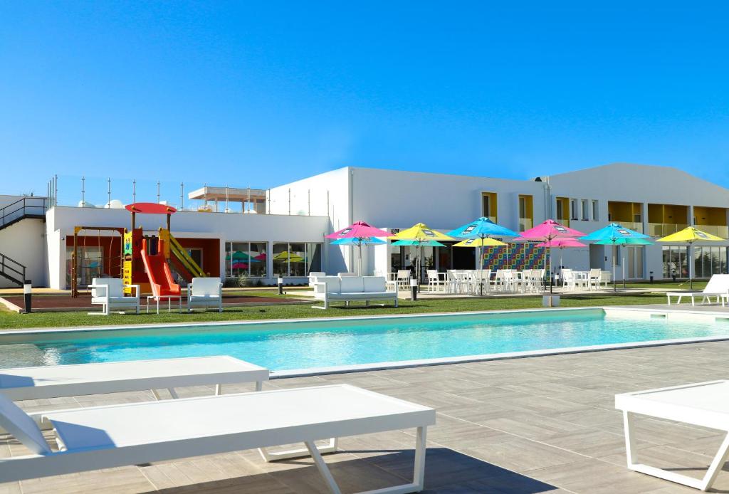 une piscine avec des chaises et des parasols, ainsi qu'une aire de jeux dans l'établissement RIDE Surf Resort & Spa, à Peniche