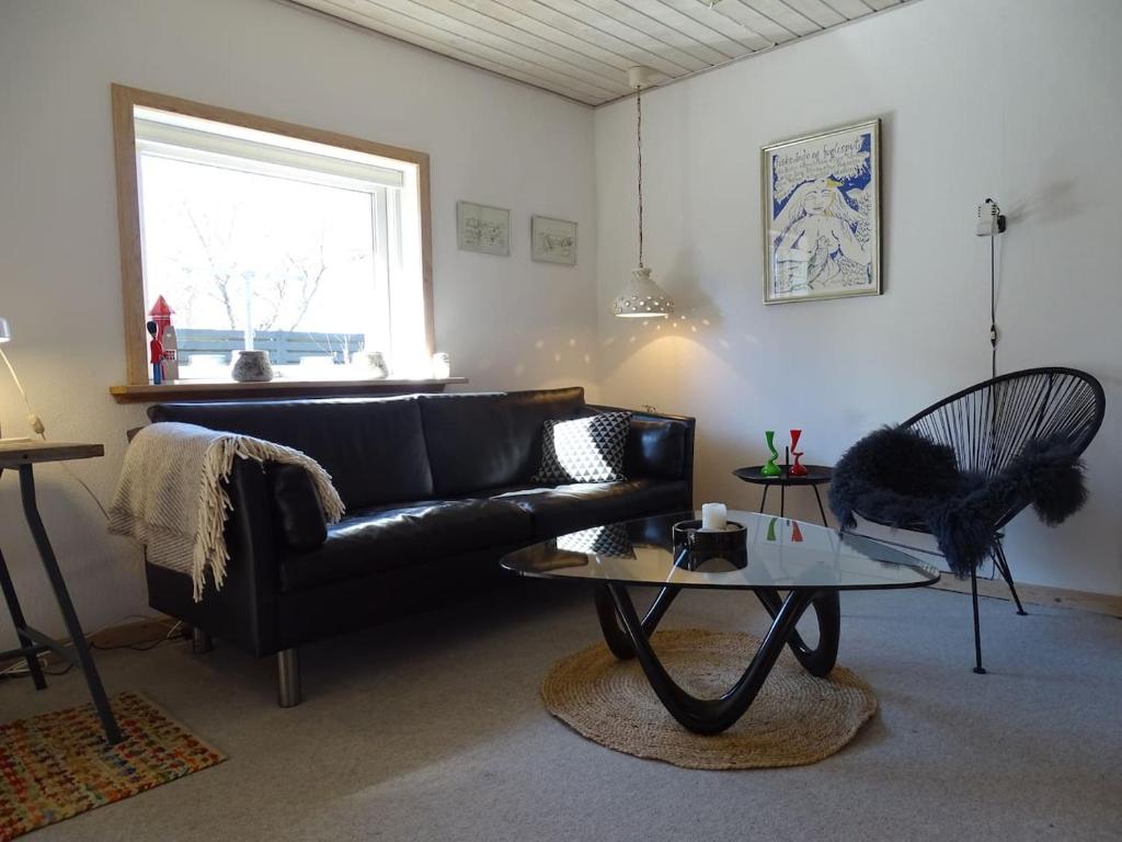 a living room with a black leather couch and a table at Fin lejlighed med lukket have in Skagen