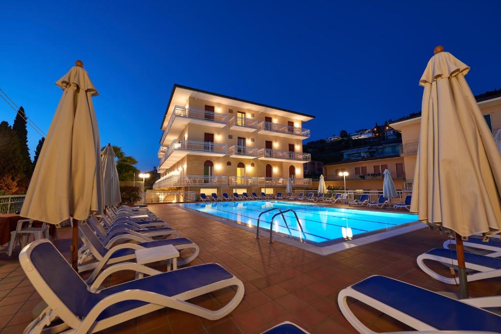 un hotel con piscina con sedie e ombrelloni di Hotel Benacus Torri del Benaco a Torri del Benaco