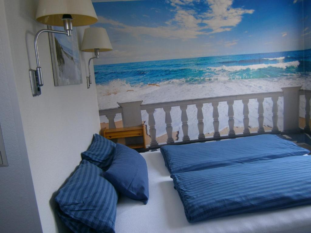 a bed with blue pillows and a painting of the ocean at Haus Steinbach in Kellenhusen
