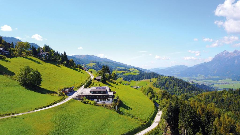 a house on top of a green hill with a road at Sonnenalm Mountain Lodge in Gröbming