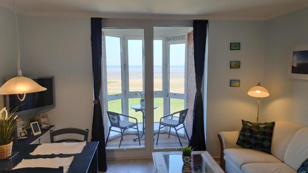 ein Wohnzimmer mit einem Sofa und Stühlen sowie einem Balkon in der Unterkunft 180° Panoramameerblick - Ferienwohnung Sandkorn in Cuxhaven