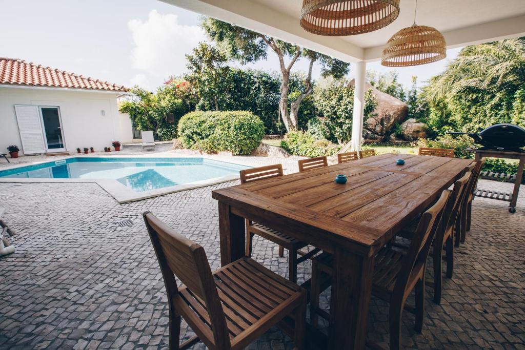 patio con mesa de madera, sillas y piscina en Sunny Soul, en Malveira da Serra