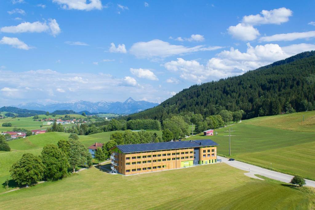 Ein Gebäude auf einem Feld mit Bergen im Hintergrund in der Unterkunft Explorer Hotel Neuschwanstein in Nesselwang