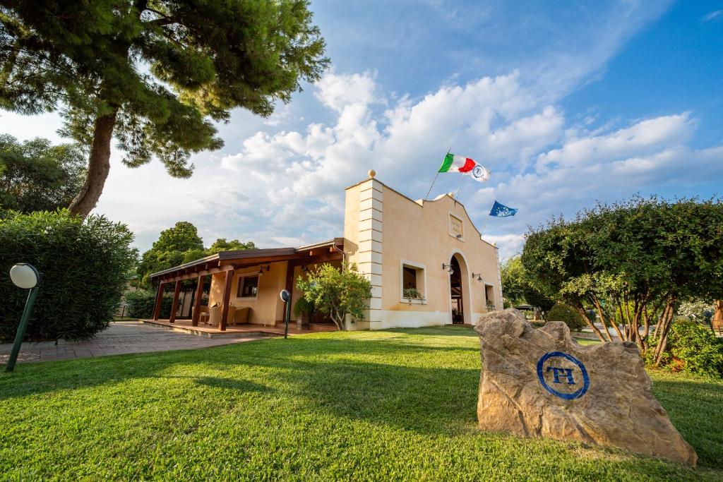a building with a flag and a rock in the grass at TH Marina di Sibari - Baia Degli Achei Village in Marina di Sibari