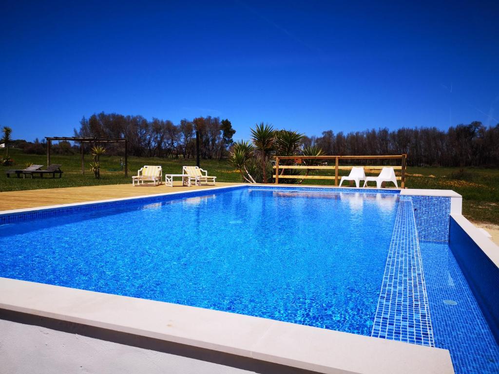 a swimming pool with blue water and two chairs at Quinta de Moledos in Aljezur