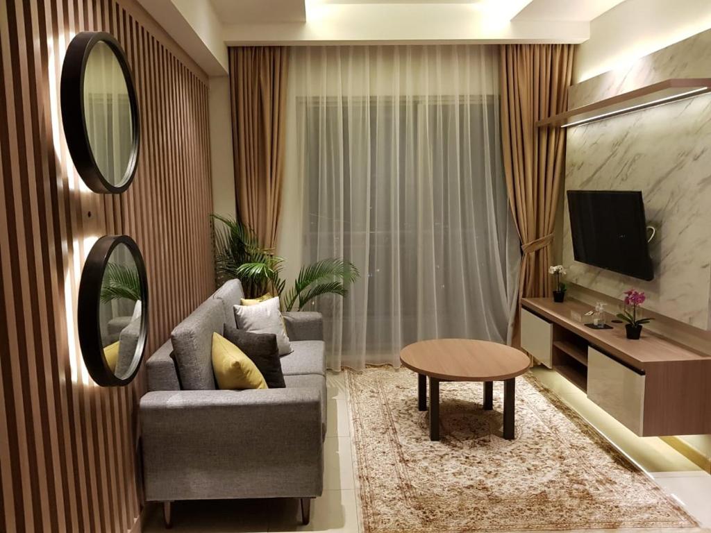 een woonkamer met een bank, een tafel en een spiegel bij M-Town Signature Gading Serpong by J`s Luxury Apartment in Pumpangsineng