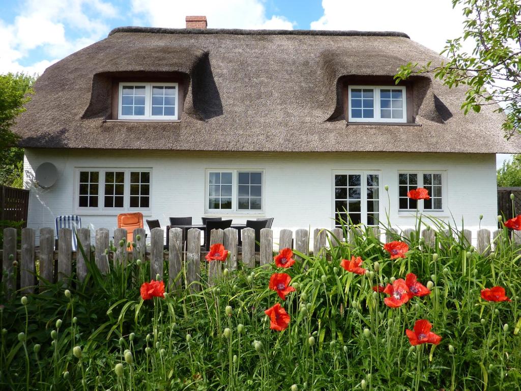 dom z dachem krytym strzechą i czerwonymi kwiatami w obiekcie Austernfischer Haus w mieście Pellworm